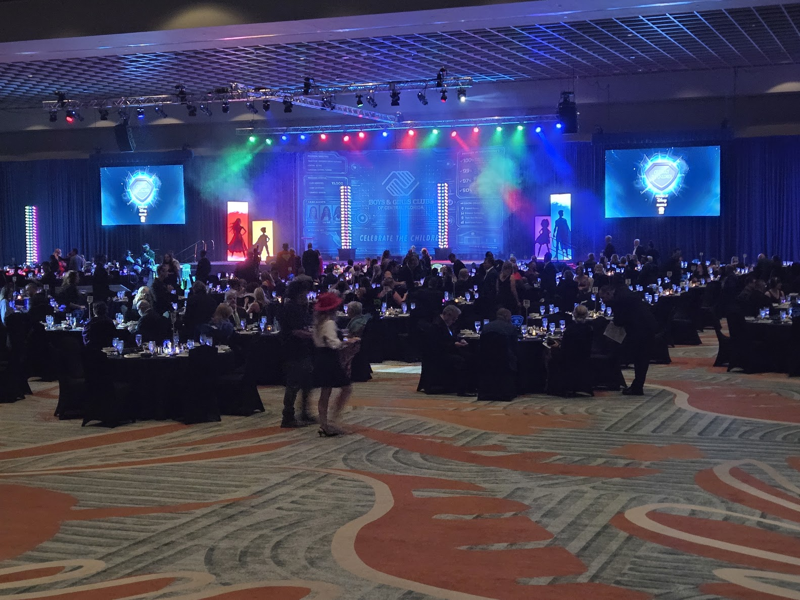 Large gala event with screens, stage lighting, and seated guests
